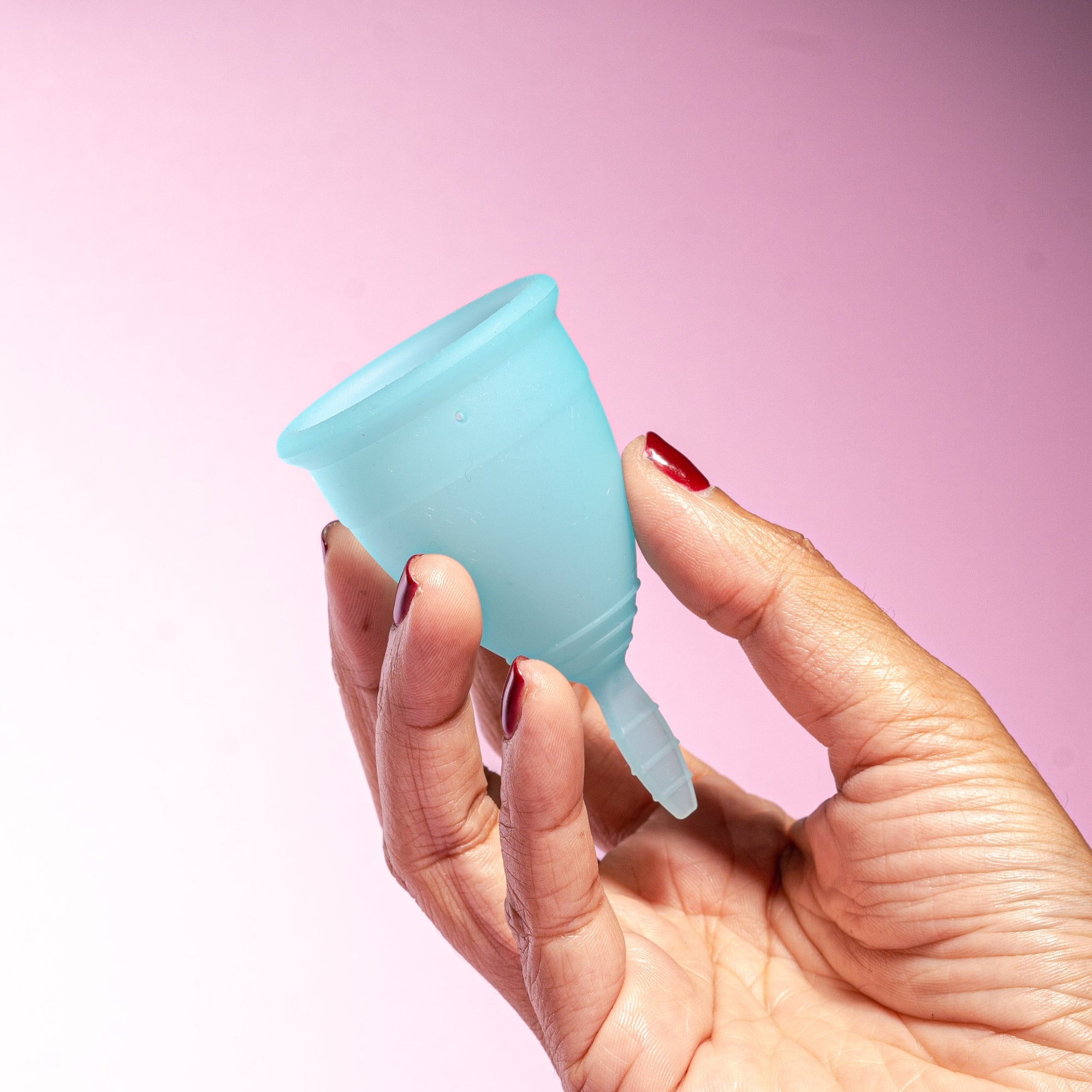 Product detail menstrual cup in soft blue color. Cup is in the fingers of a person with dark red nail color
